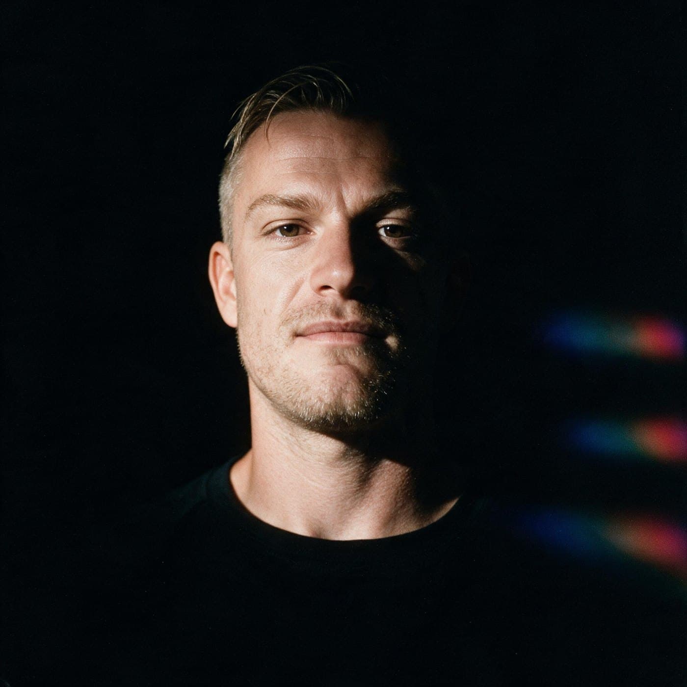 Portrait of Alex Collins, lit from one side with a spectrum light leak